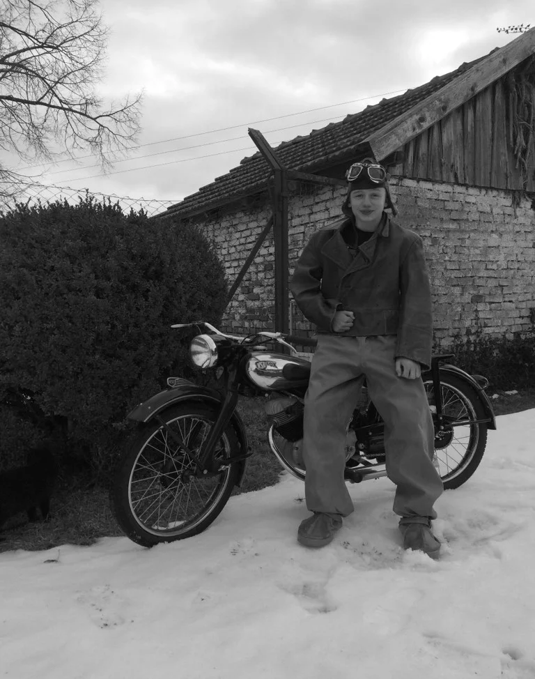 Ein schwarzweiß-Bild zeigt einen Azubi mit Lederhose auf einem Motorrad.