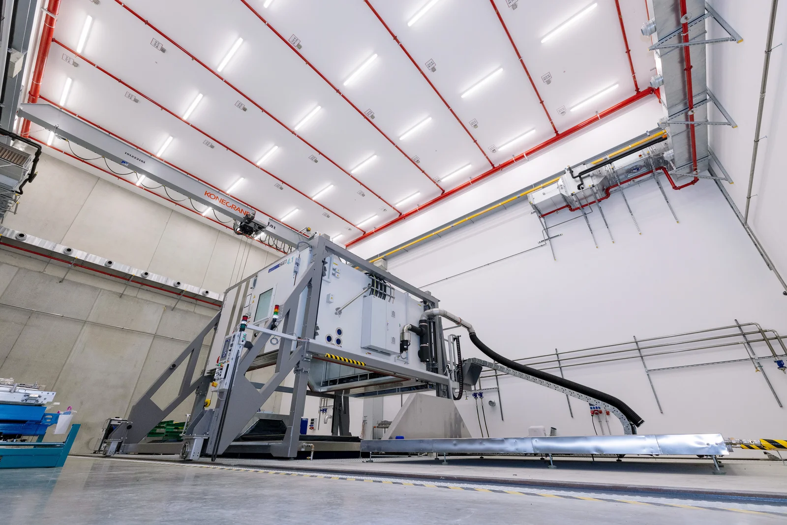 Große Industriemaschine in einer geräumigen Anlage mit hohen Decken und verschiedenen Rohren und Kabeln.