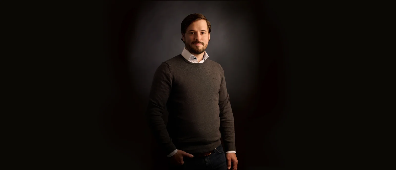 A man in front of a black background smiles into the camera with his arms crossed.