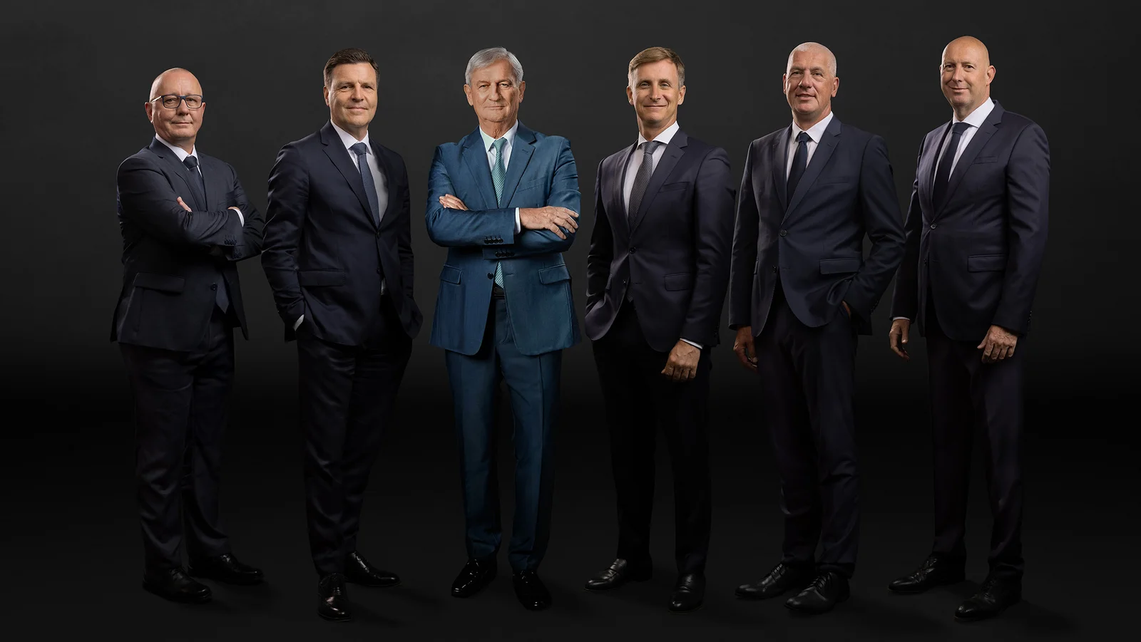 Die Hauptgeschäftsführung vor schwarzem Hintergrund. Sechs Männer lächeln in die Kamera.