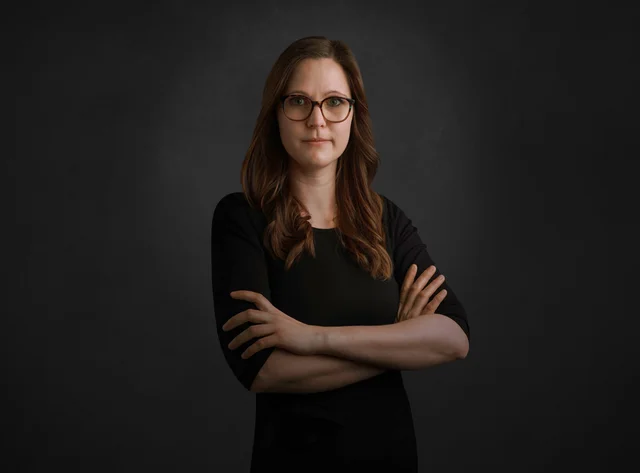 Bianca Eine Frau mit Brille steht mit verschränkten Armen vor schwarzem Hintergrund.