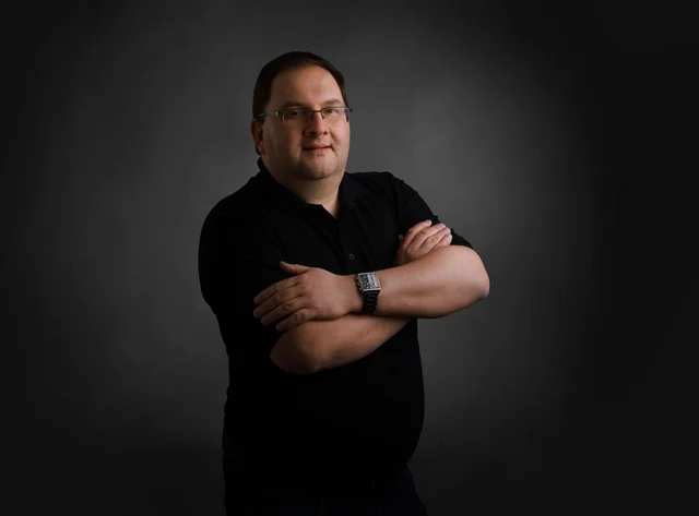 Eugen Ein Mann mit Brille steht mit verschränkten Armen vor schwarzem Hintergrund.