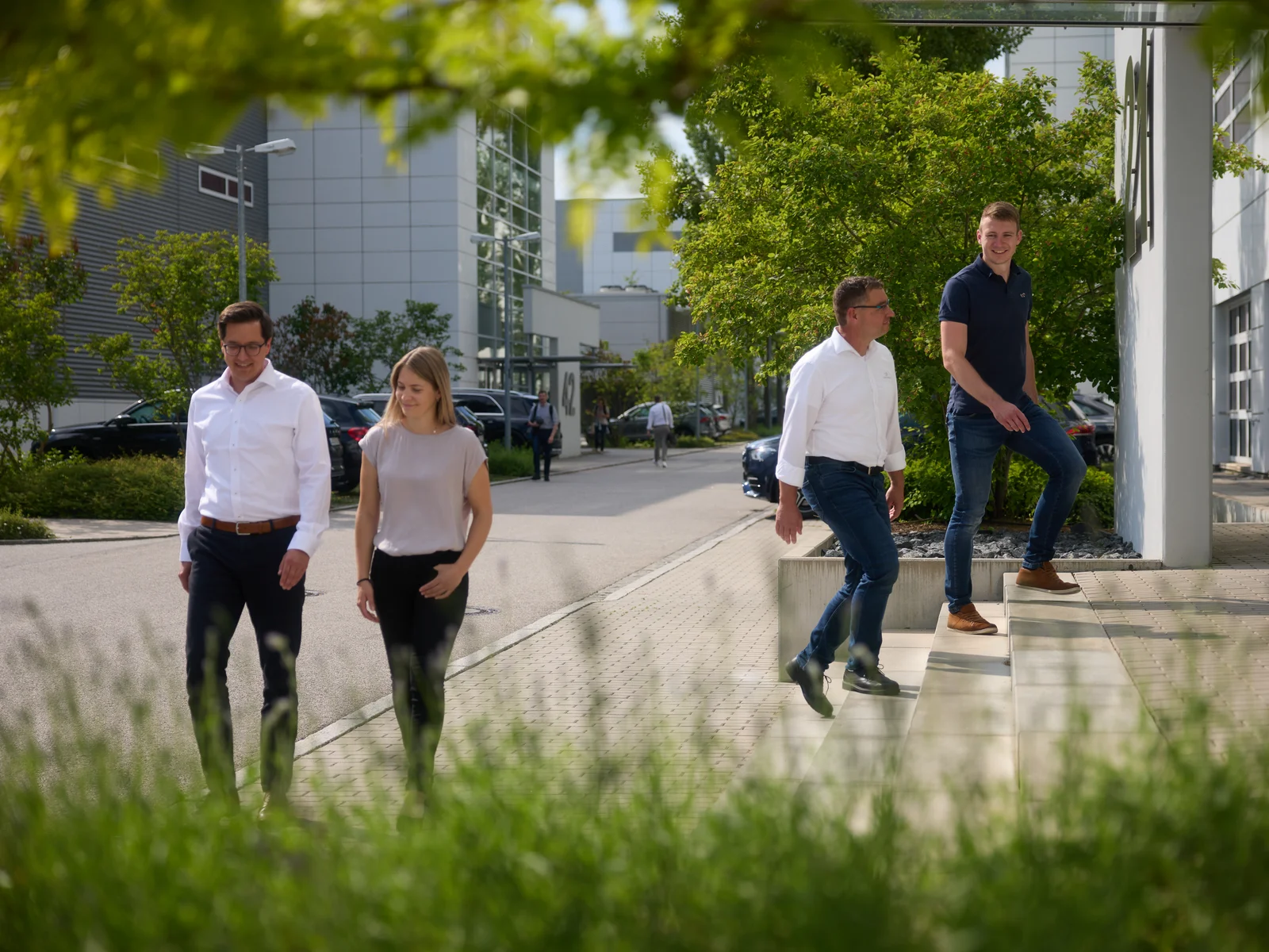 Vier Personen unterhalten sich auf dem DRÄXLMAIER Gelände. Im Hintergrund grüne Bäume.