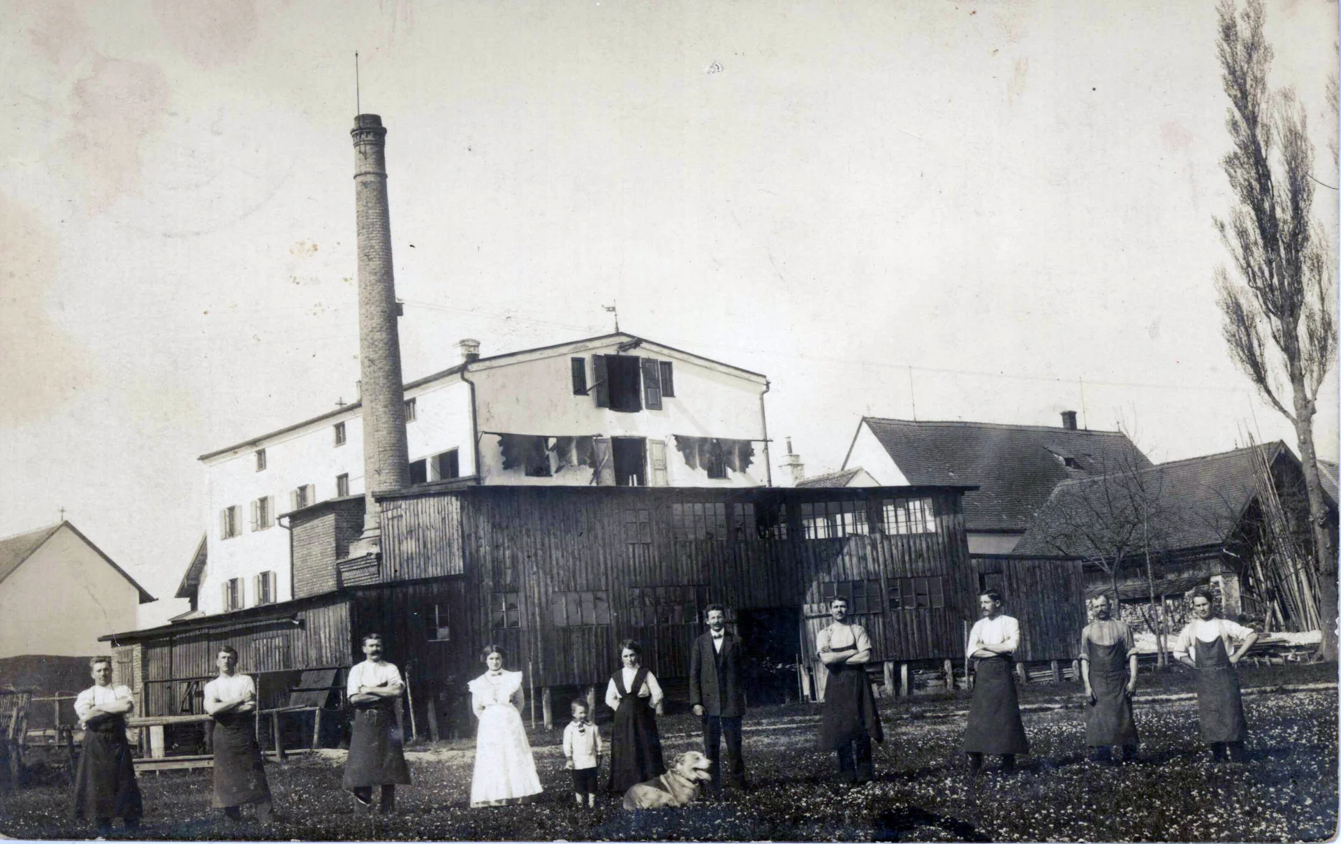 A black and white picture shows an old building in Geisenhausen. Eleven people and a dog are standing in front of it.