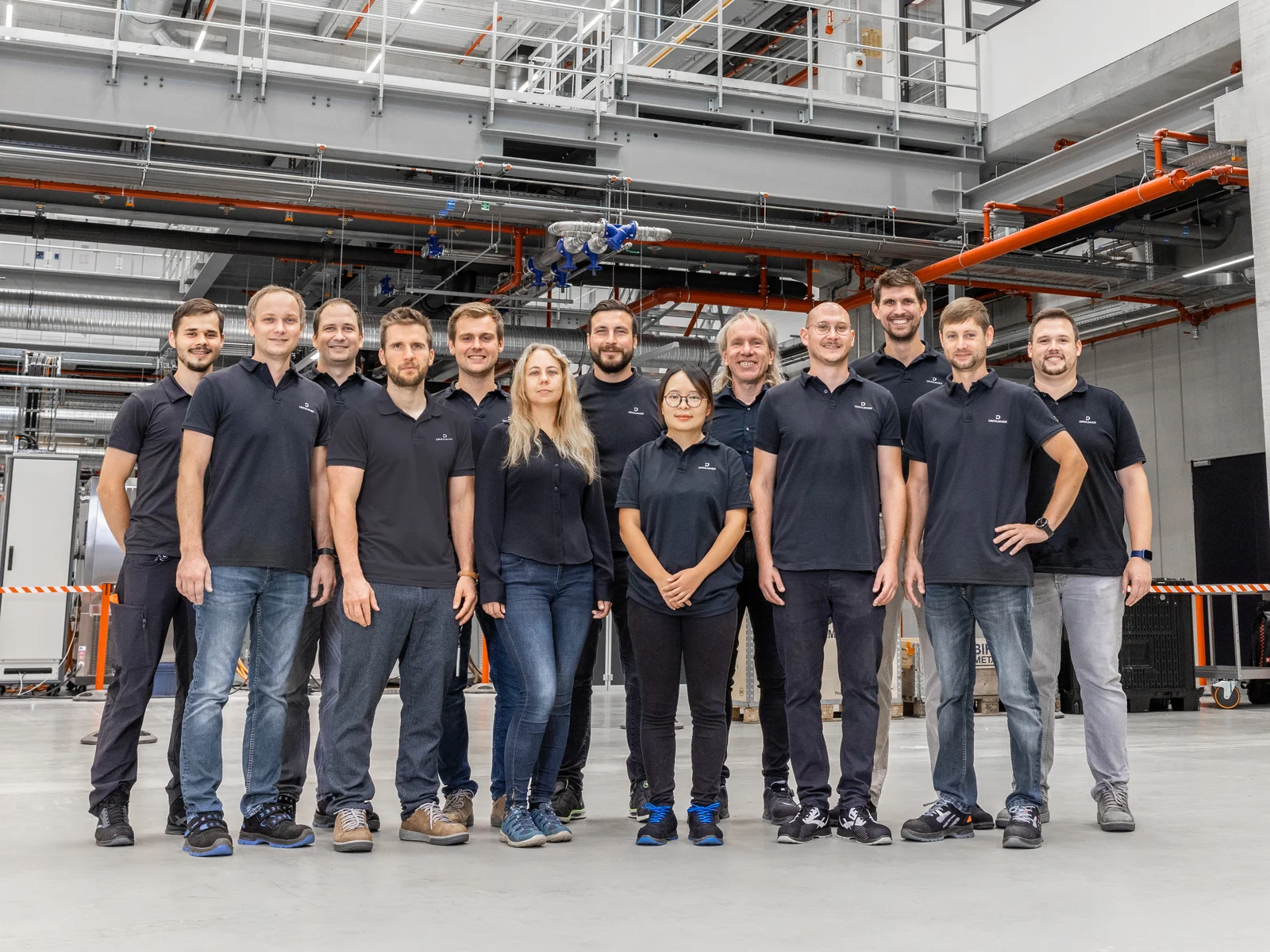 Ein Gruppenfoto mit lächelnden DRÄXLMAIER Produktionsmitarbeitern in einer Halle.