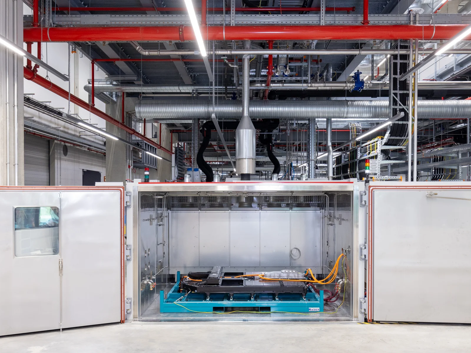 Industrial environment with a large machine in the center and various pipes and cables on the ceiling.