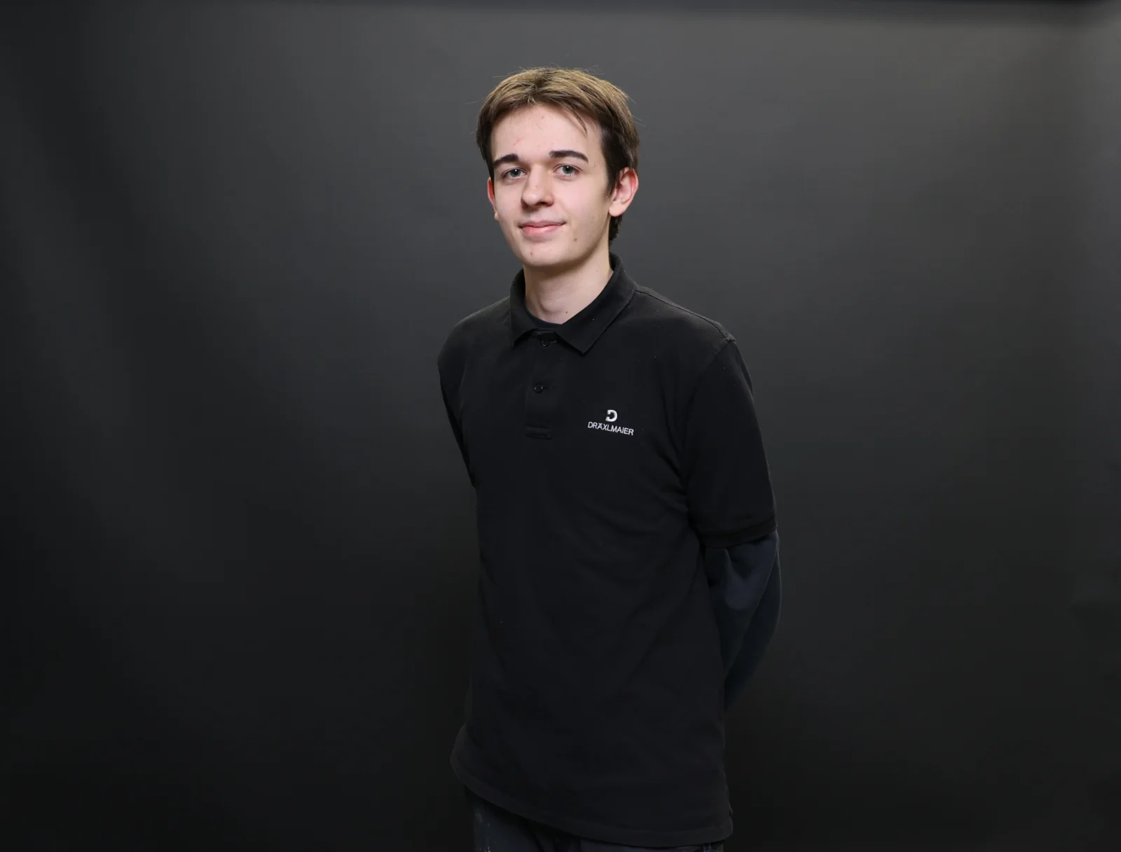 A trainee has his arms crossed behind his back and smiles at the camera.