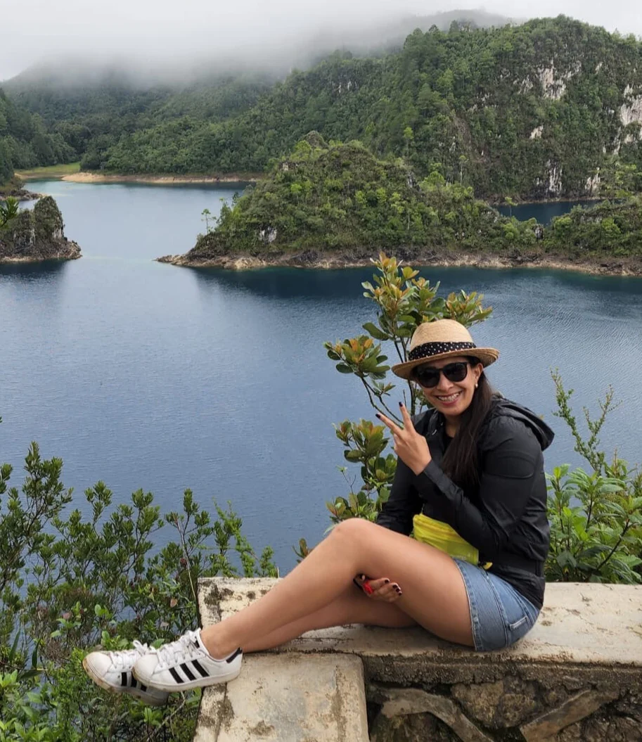 A woman sits on a ledge overlooking a lake.