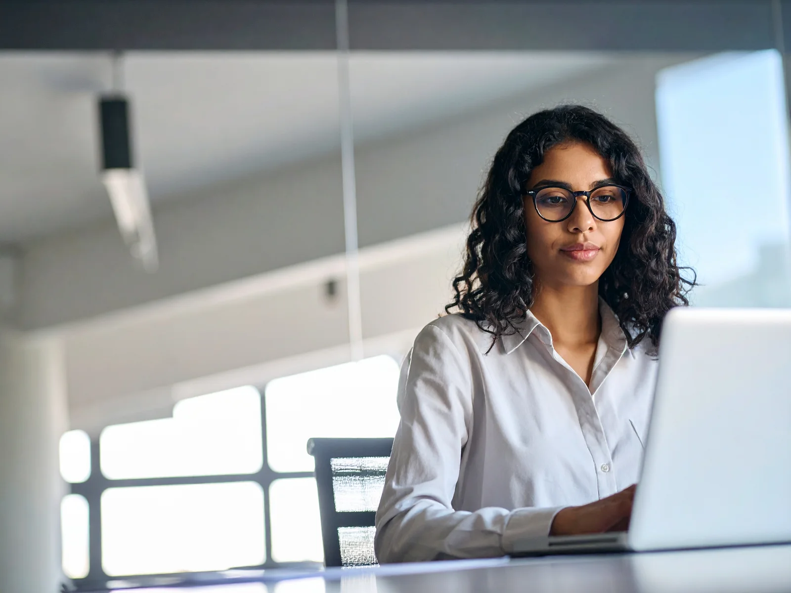 Young woman with glasses focuses on her laptop