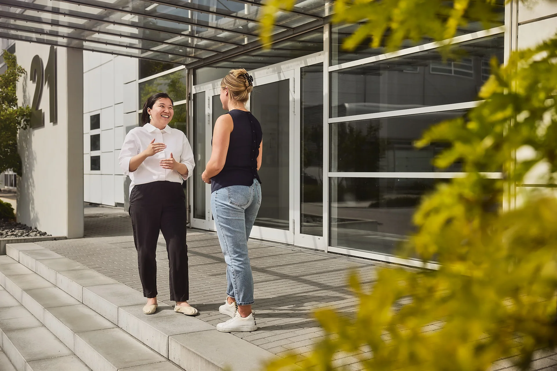 Two women are standing in front of a DRÄXLMAIER building and talking.