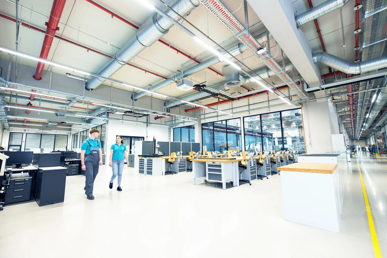 Zwei Auszubildende gehen durch die große Ausbildungswerkstatt und schauen sich währenddessen an.