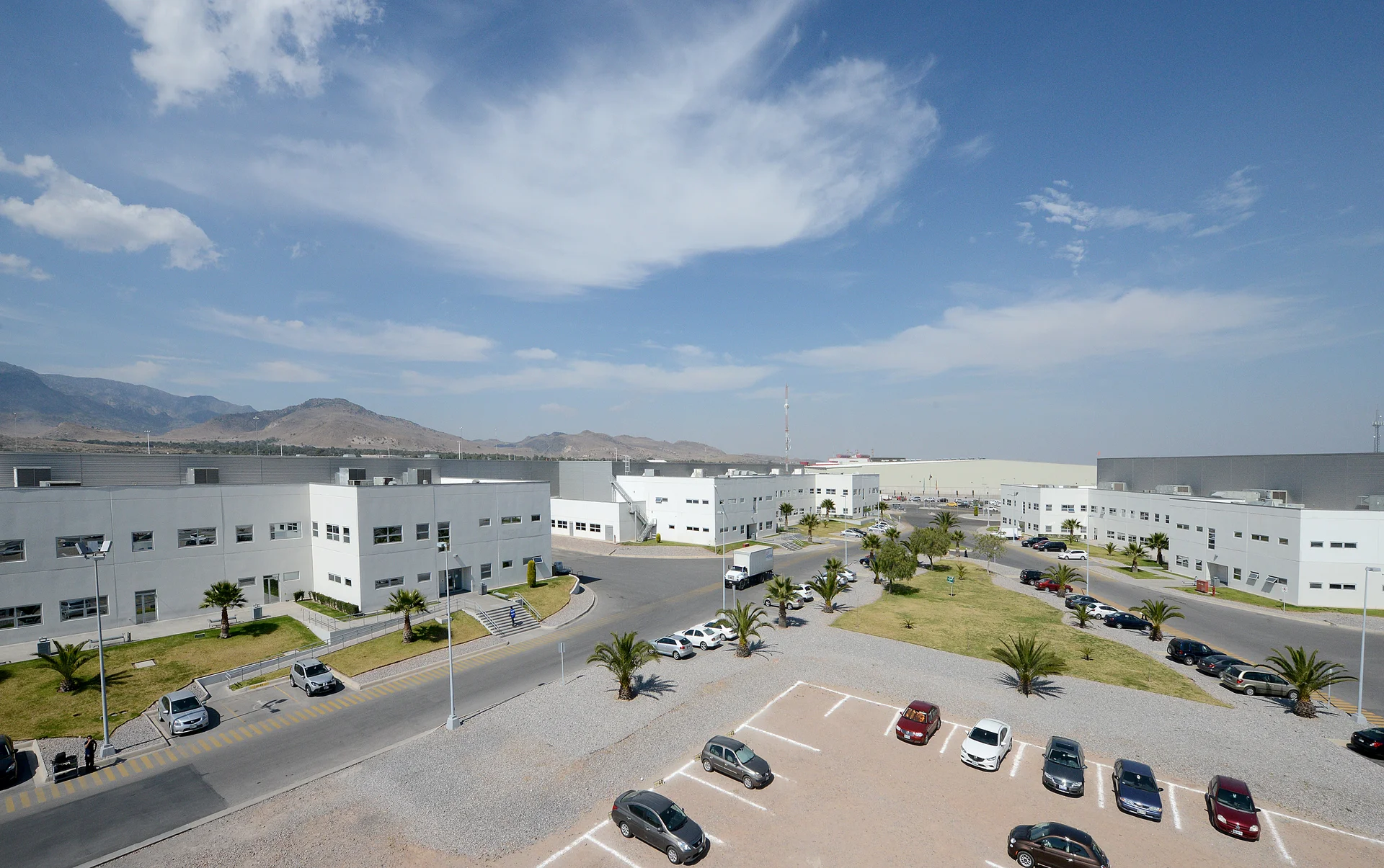 A picture of the DRÄXLMAIER buildings in San Luis Potosi. Blue sky and palm trees can be seen.